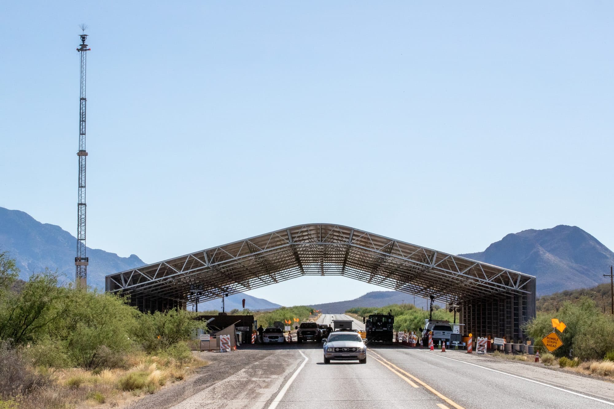 A car approaching a covered US Border Patrol highway checkpoint in desert hills.