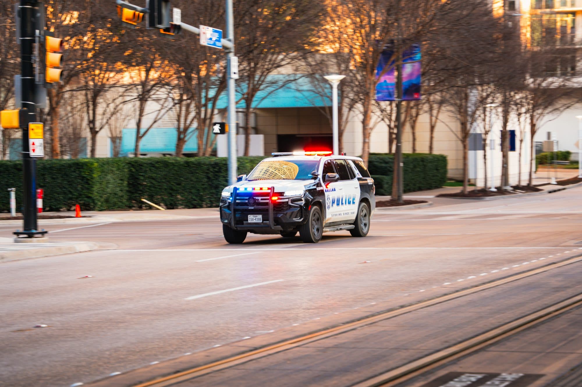 A Dallas Police SUV with its emergency lights on, driving down a downtown Dallas street.