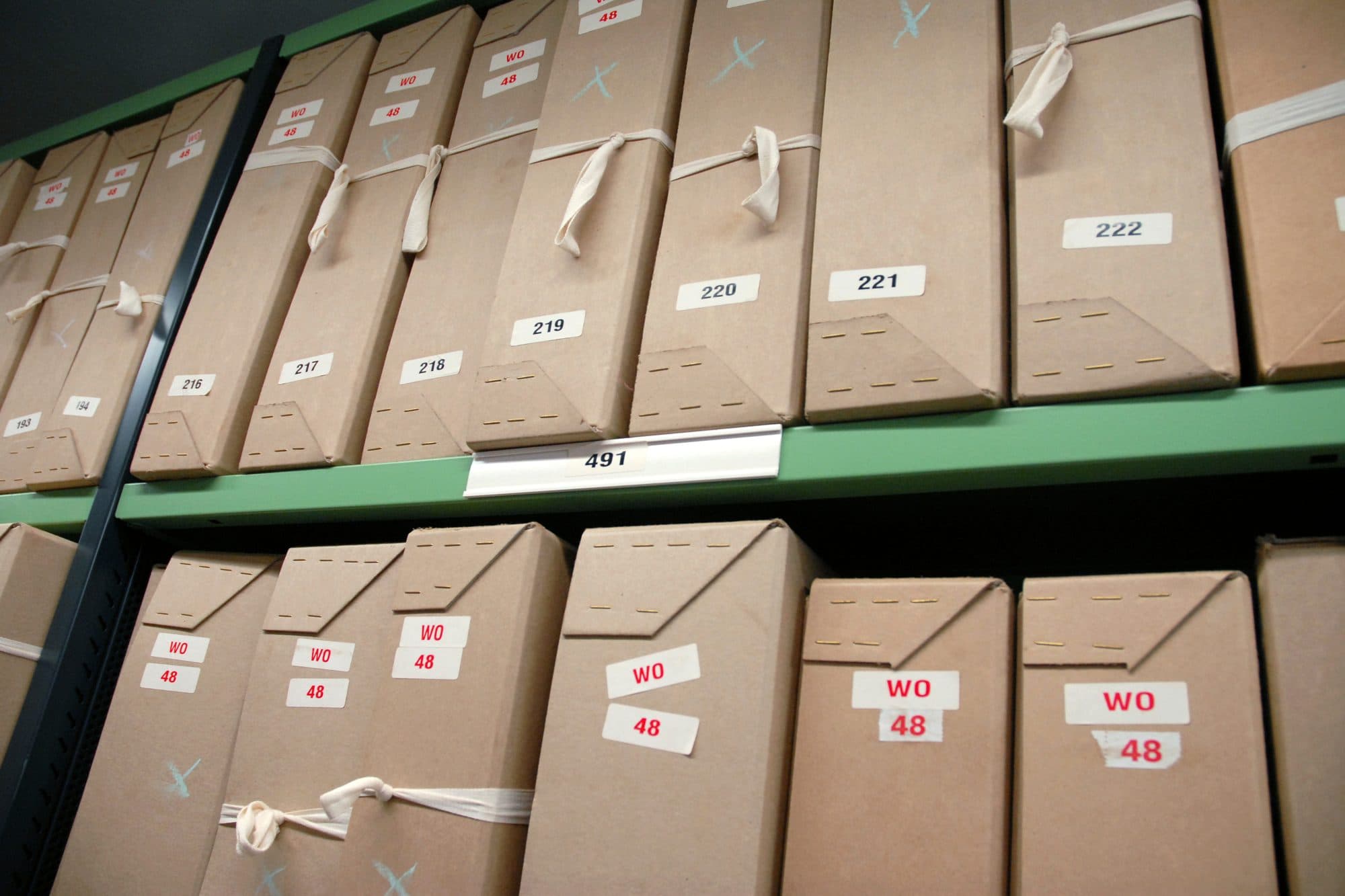 Rows of numbered cardboard document boxes on archive shelves.