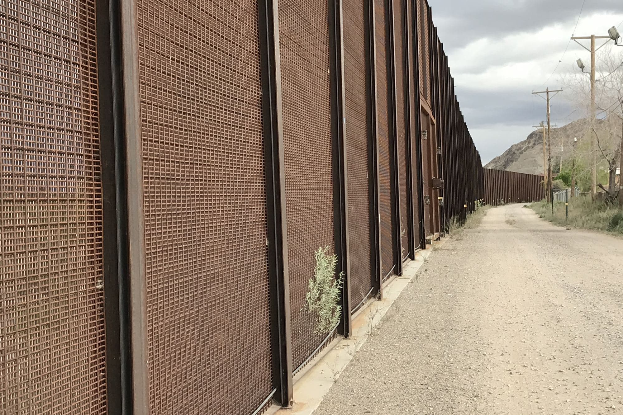 A dirt service road running beside the tall steel border fence in El Paso.