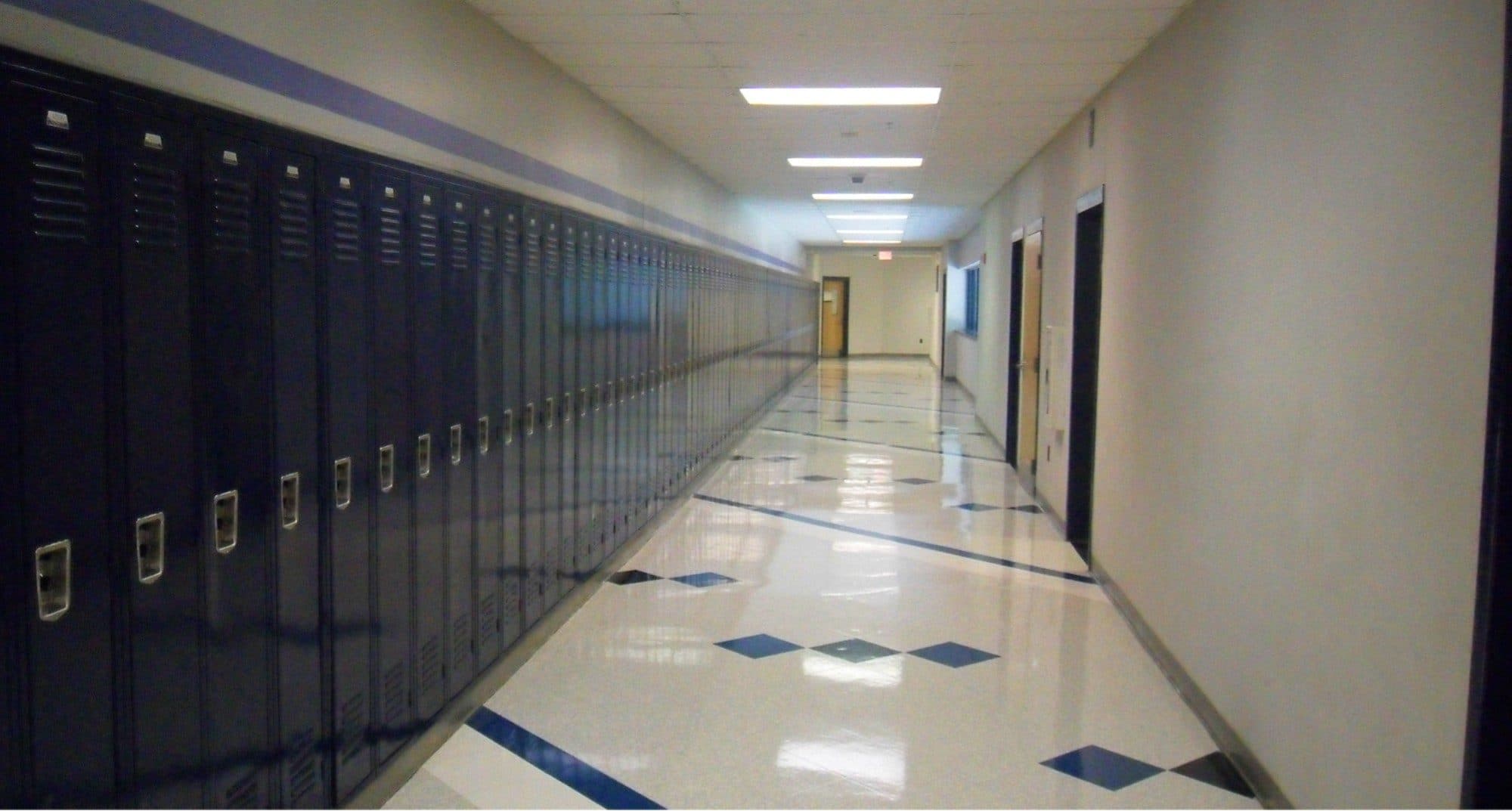 An empty school hallway lined with dark blue lockers and a shiny tiled floor.
