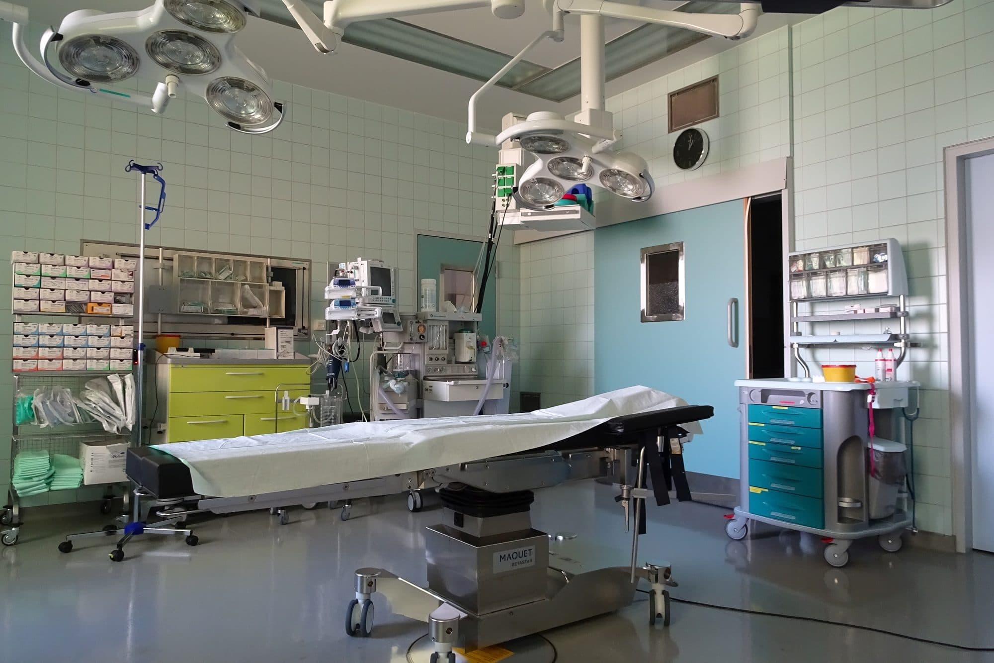 An empty, clean hospital operating room with surgical lights above the table.