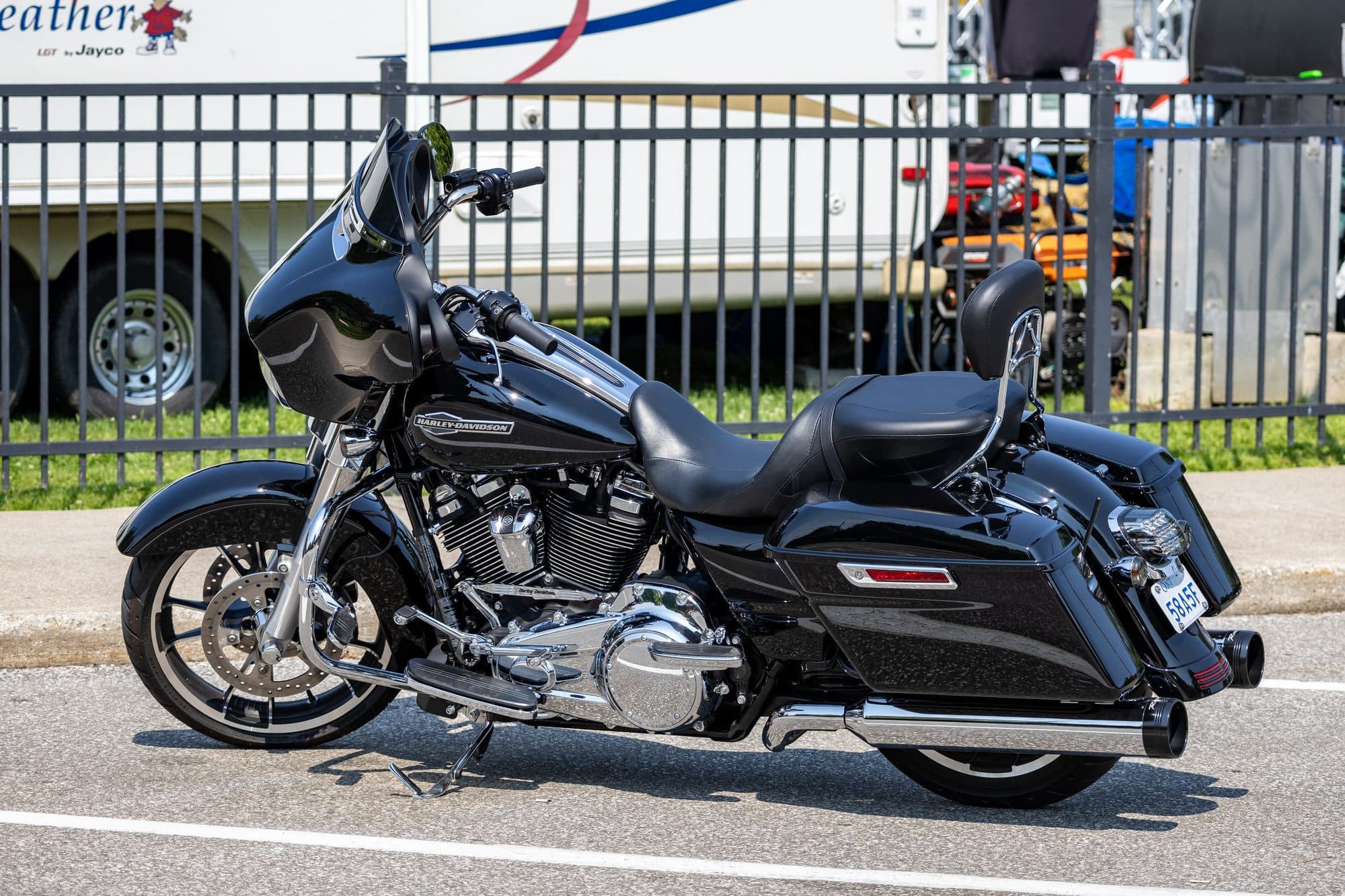 A black touring motorcycle parked along a curb next to a fence.