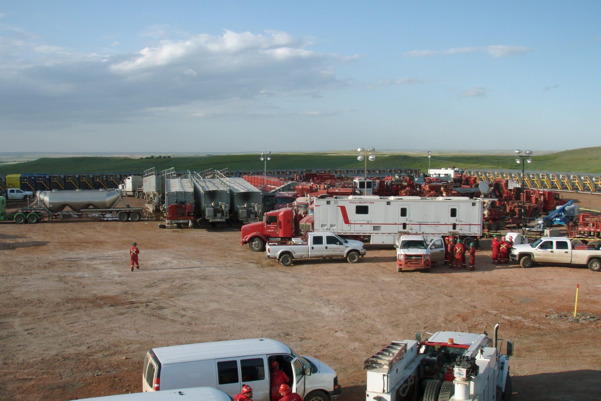 Rows of frac trucks, tankers and white pickups parked at a well site before a fracking job.