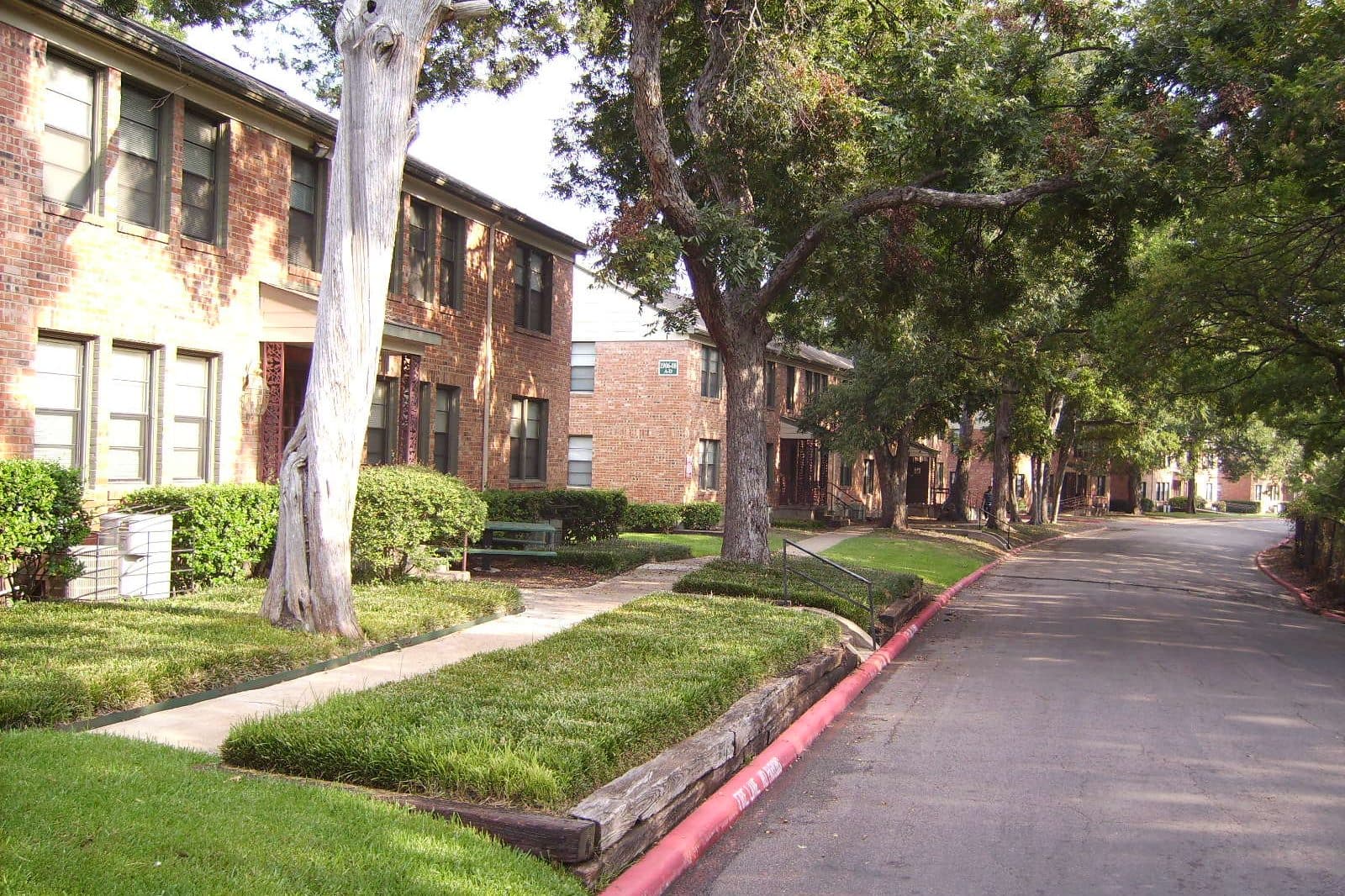 A shaded driveway between two-story brick apartment buildings at Wynnewood Park in Oak Cliff, Dallas.