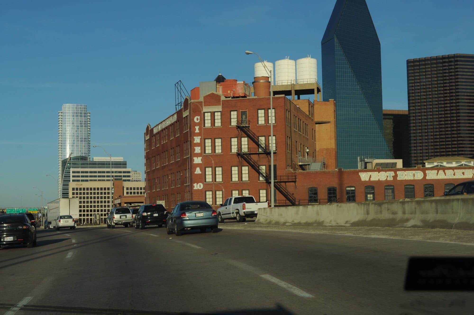 Cars heading east on Woodall Rodgers Freeway past the brick buildings of the West End in downtown Dallas.