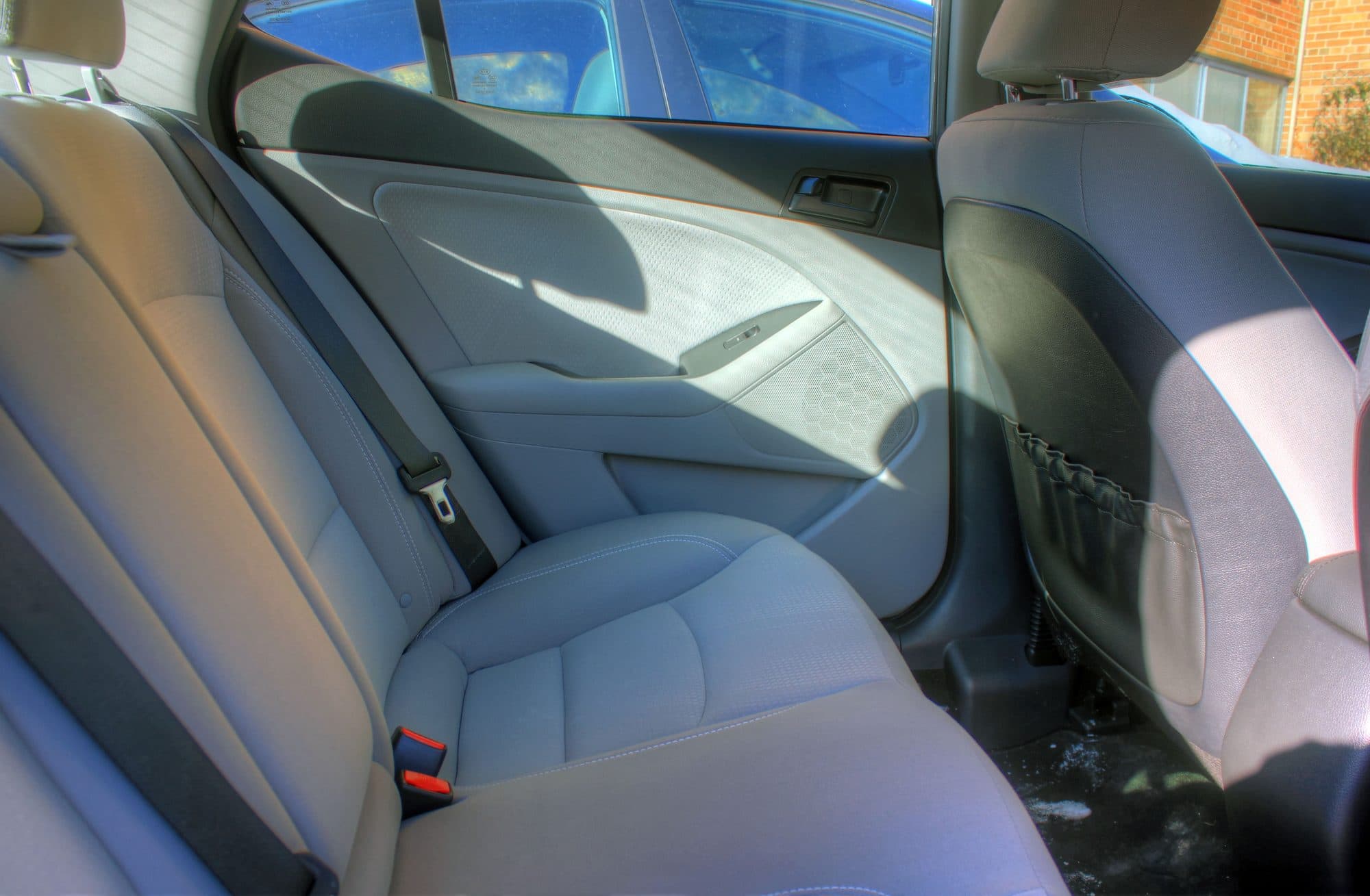 The empty gray back seat of a sedan, seen through the open rear door.