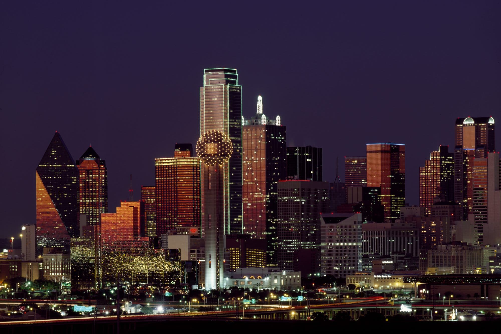 The downtown Dallas skyline at dusk under a deep purple sky, with Reunion Tower lit up.