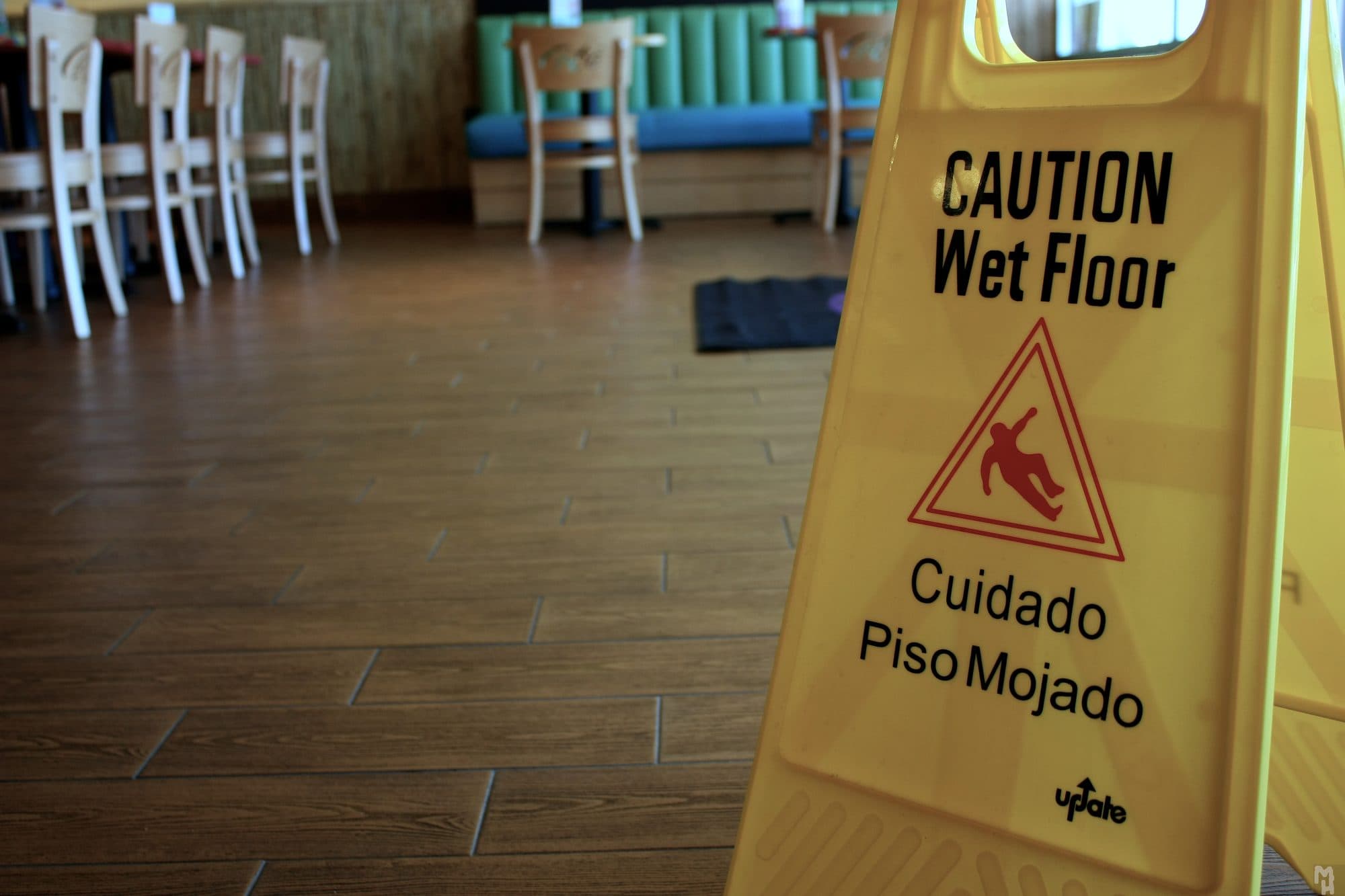 A yellow bilingual wet floor sign reading Caution Wet Floor and Cuidado Piso Mojado on a restaurant floor.