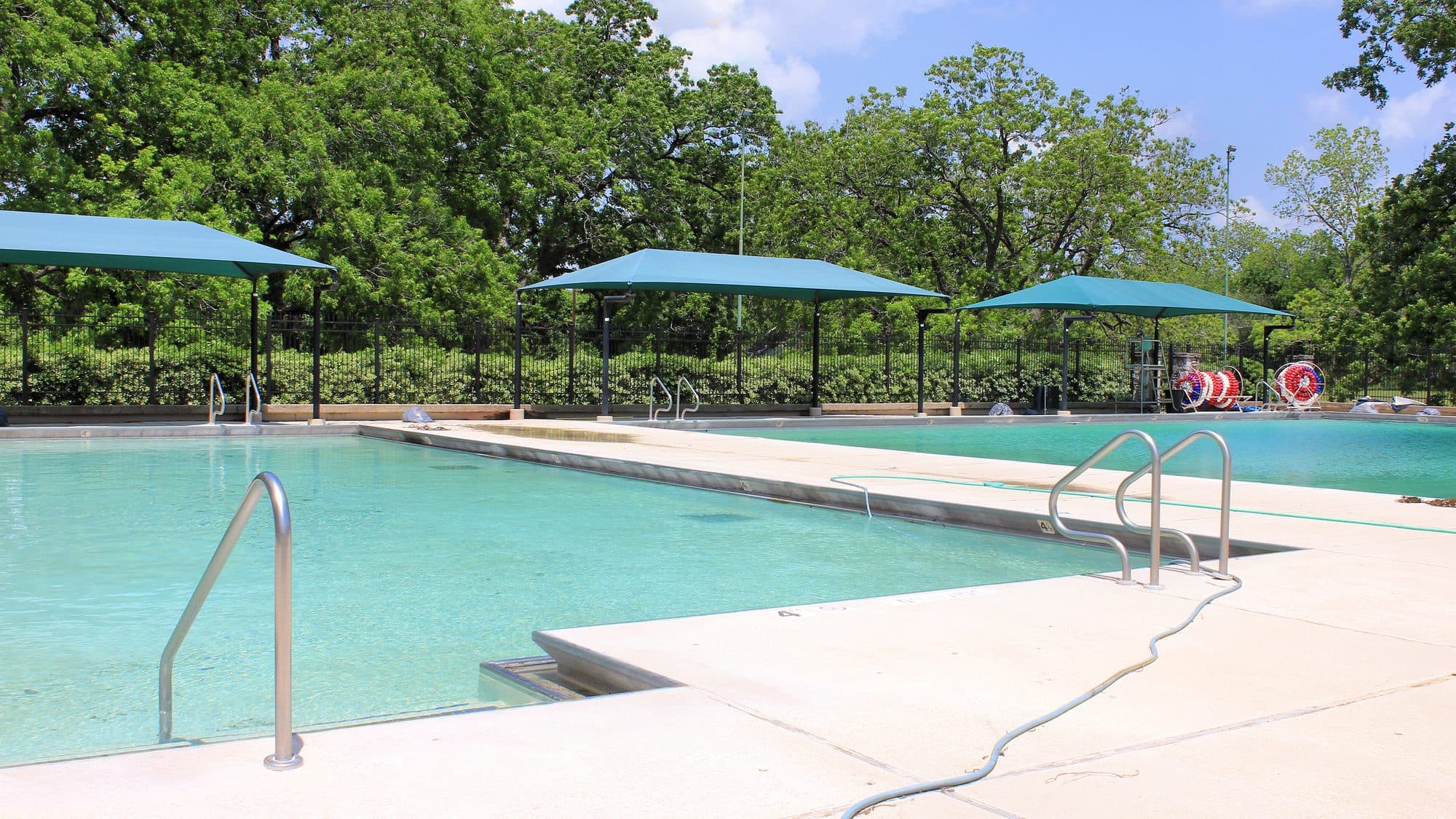 An empty outdoor public swimming pool with metal ladders and shade canopies in Navasota, Texas.