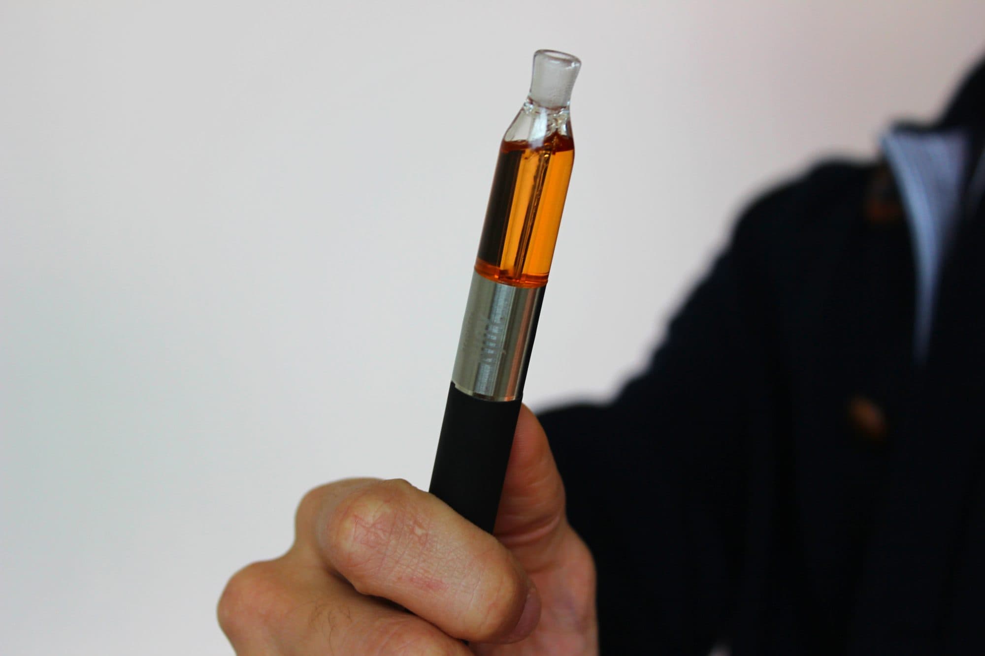 A hand holding a vape pen with an amber liquid cartridge.