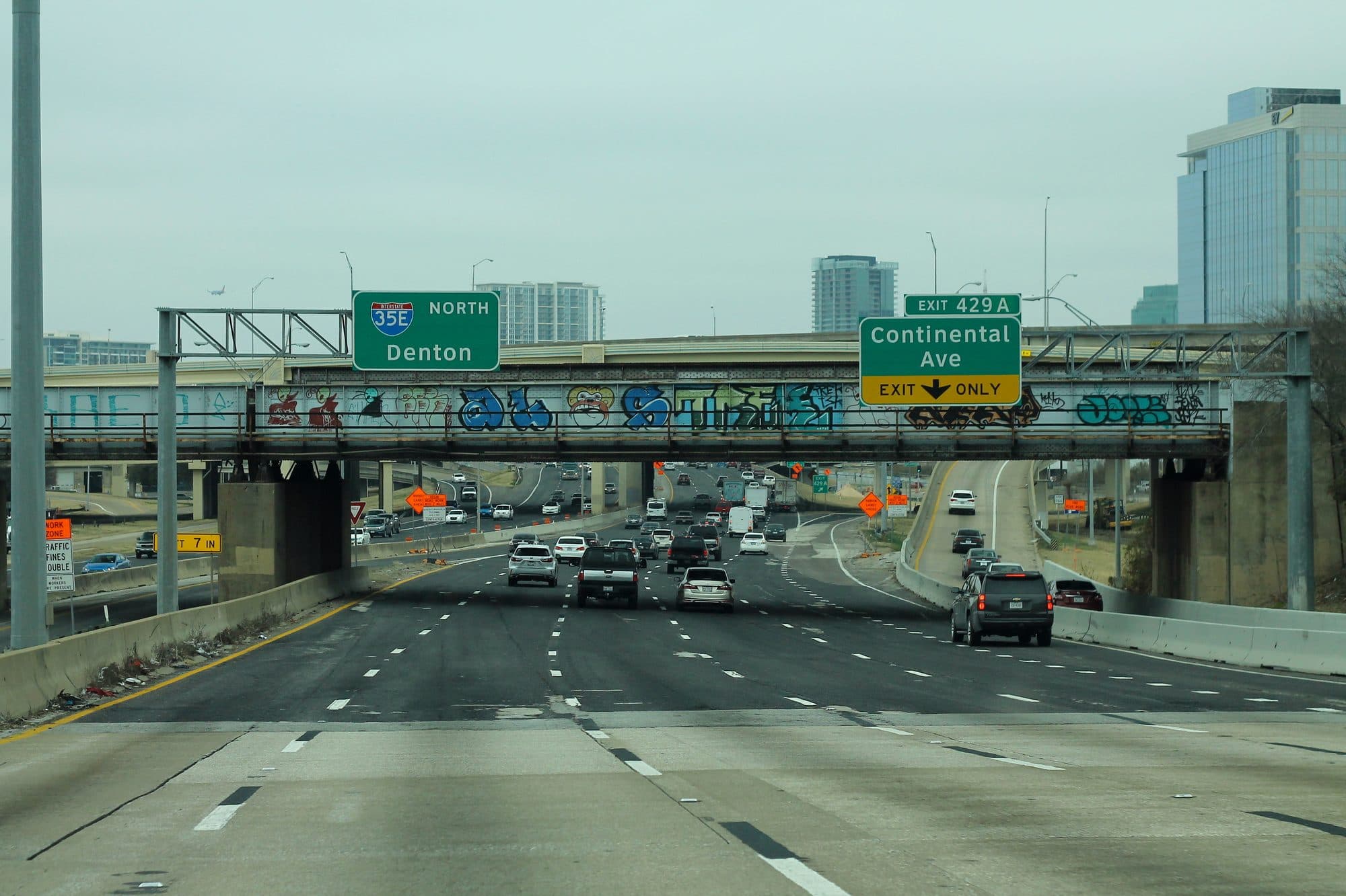 Traffic heading north on I-35E in Dallas under green exit signs for Denton and Continental Avenue.