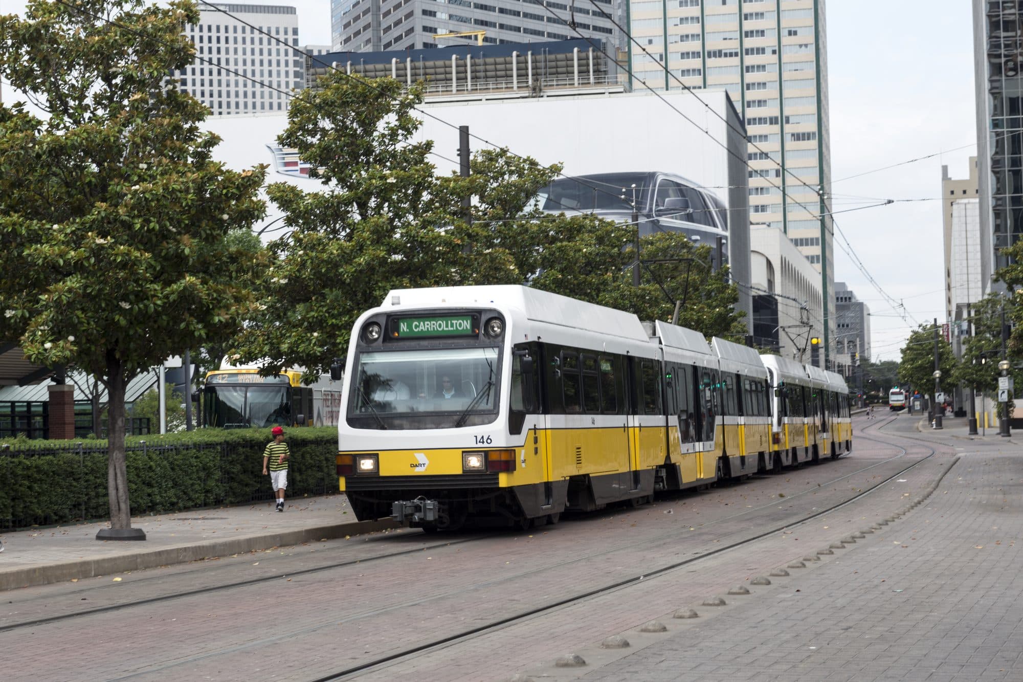 A DART light rail train moving along a downtown Dallas street between office towers.